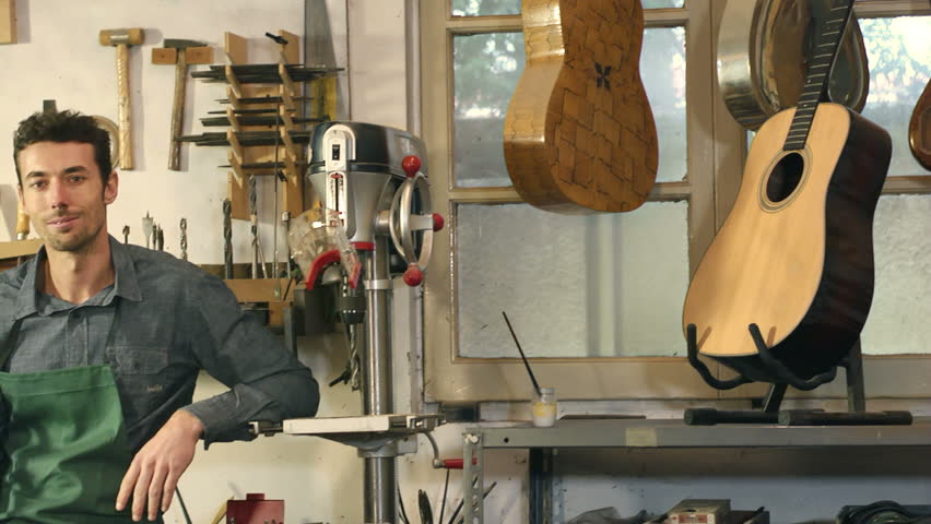Portrait of man at work as craftsman in Italian music shop with tools, bass, guitar and musical instruments