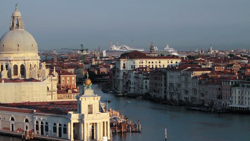 Venice Italy canal and lagoon passing by the Santa Maria delle Salute basilica cathedral. Early morning light. Cruise ship in distance at marina port. Video capture from moving ship at high angle