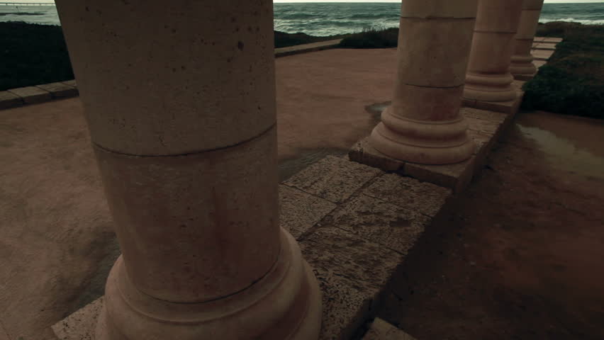 Close-up wide tilt up four columns from the palace ruins at Caesarea Maritima, Israel.  The Mediterranean Sea and the cloudy sky nearing sunset make a beautiful background.