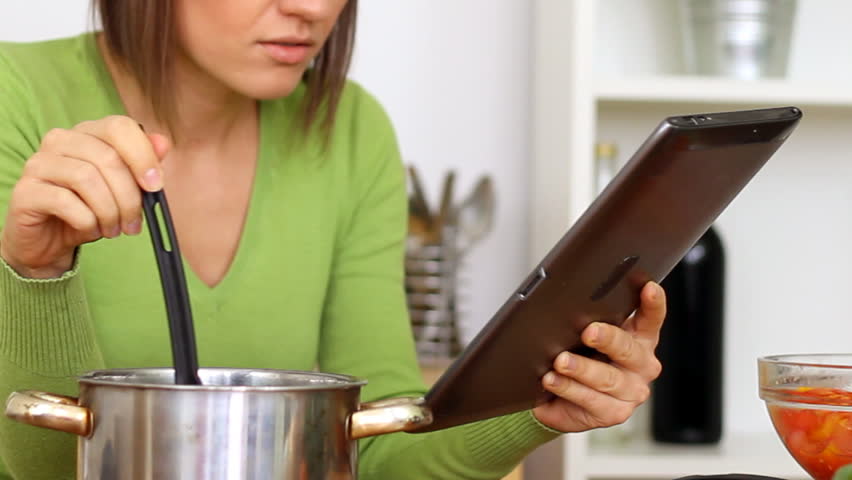 Woman cooking and looking at recipe on digital tablet