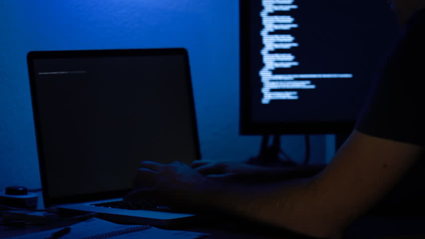 hacker at night in a dark blue illuminated office trying to breach into a computer system