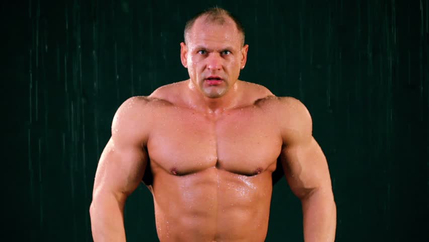 Bodybuilder stands under water jets, he gets into few poses with muscular tension