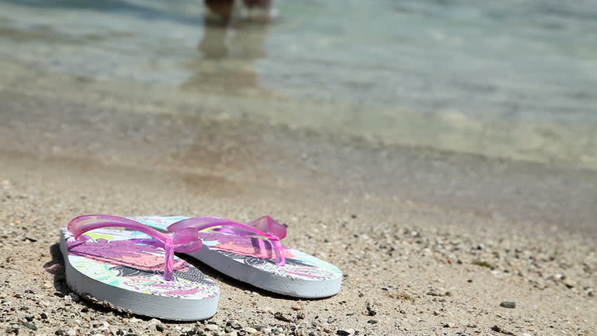 female feet walking out of sea wearing flip flops and leaving