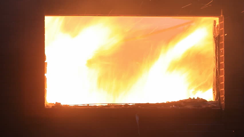 Fire burning with intense fire and flames at night inside a house burning with flames and smoke coming through broken window.