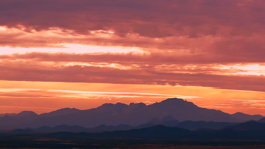 Time Lapse, Clouds in Arizona sky, streaked red by setting sun, glide across silhouetted mountains. 1080p