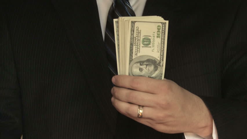 A businessman in a suit counts hundred dollar bills in front of him 