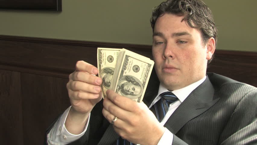 A businessman in a suit counts hundred dollar bills in his office 
