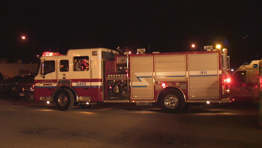 Side view of fire engine parked at night, lights flashing while ambulance arrives behind 