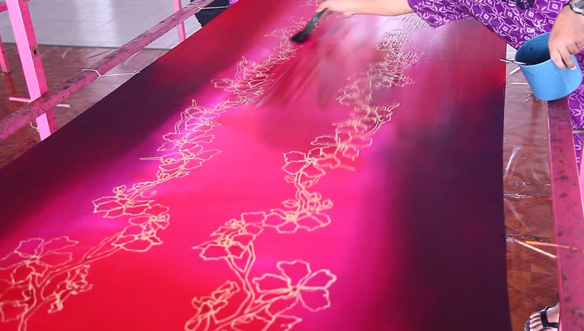 An artist paint a base reddish purple color on beautiful batik fabric with flower motif