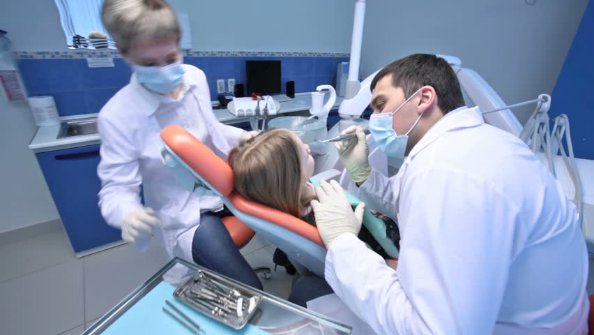 Dentist treating a little patient, assistant helping him, camera moving forward and back
