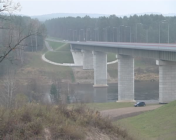 Large high bridge over flowing river water and cars ride it. Architectural decisions.

