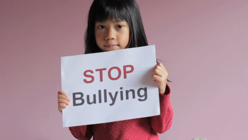 A sad 6 year old Asian girl holds a "stop bullying" sign.