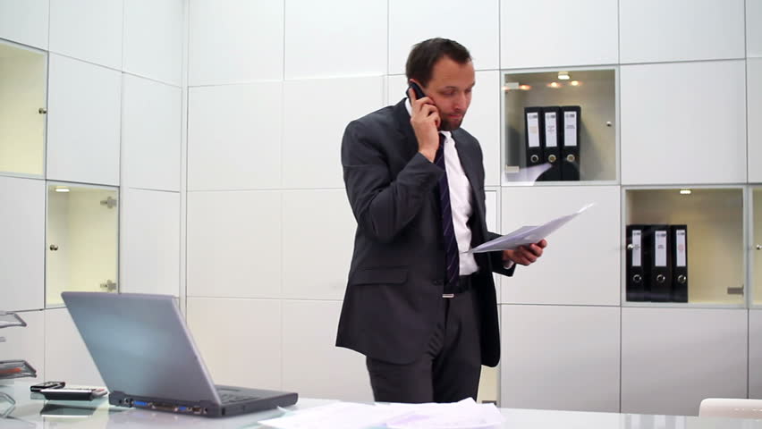 Businessman with documents talking on cellphone in modern office