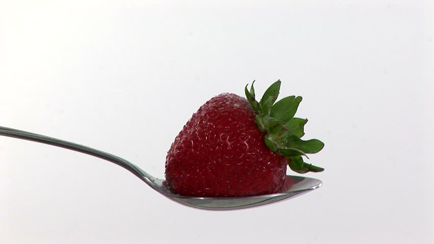 A strawberry on a spoon being covered with chocolate