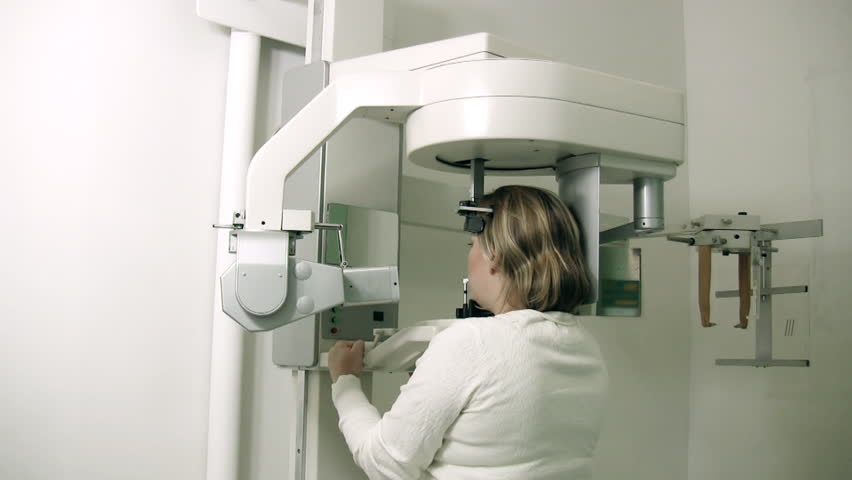 Panoramic Radiology Machine (HD). Woman standing still while X-Ray machine exposes plate to generate a dental panoramic slide. 