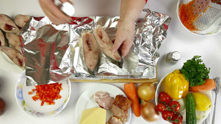 Female hands cooking baked fish - add salt and pepper Shoot from above