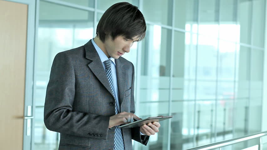 Serious businessman using a pad searching for information then looking at camera with a smile