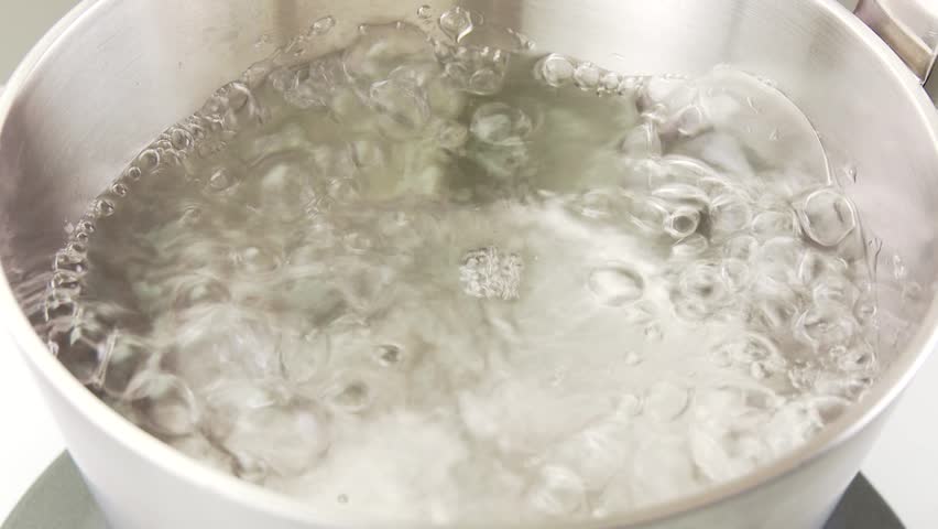 An egg being placed into a pot of boiling water