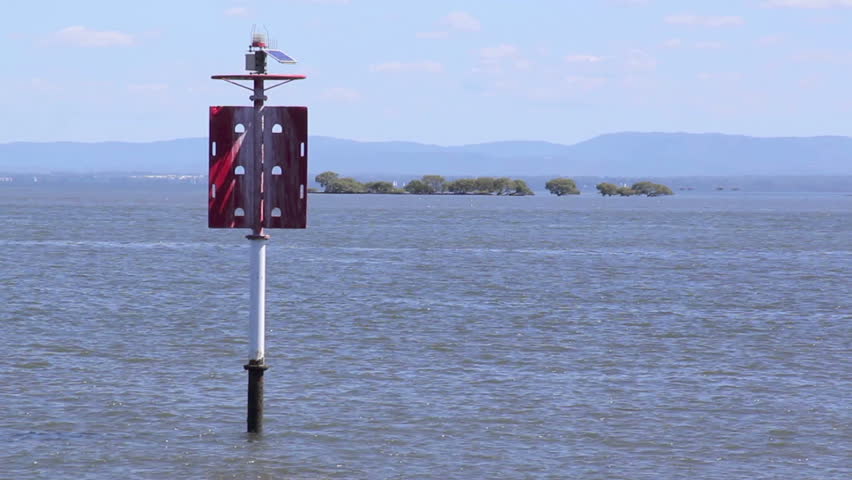 Two speed boats pass behind a red beacon on open water.