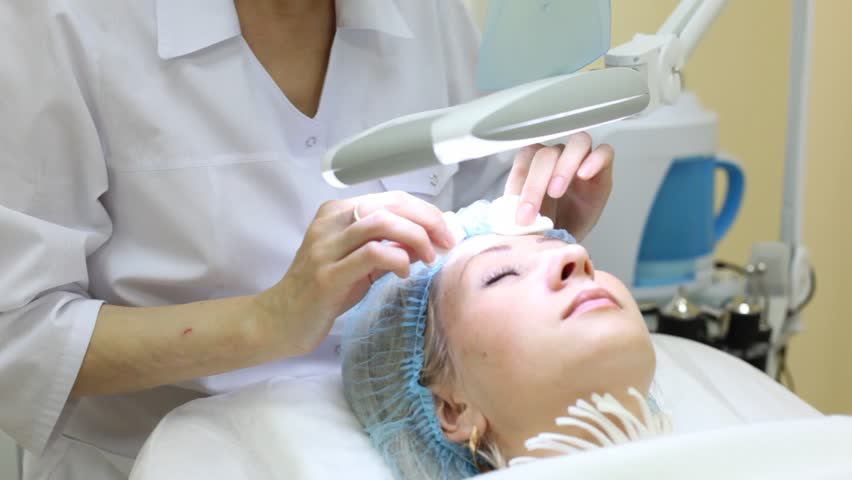 Beautician does disinfection of forehead by cotton pads after cosmetic procedures to client
