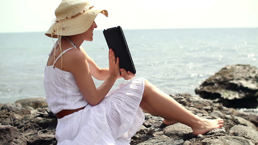 Young woman chatting on tablet computer on rocks by the sea