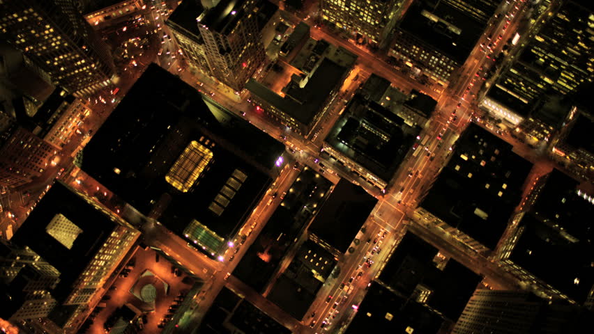 Aerial night vertical view of skyscraper rooftops and illuminated streets in a modern city