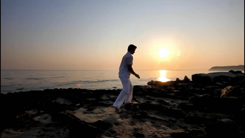 Handsome man practicing thai chi on the beach at sunrise
