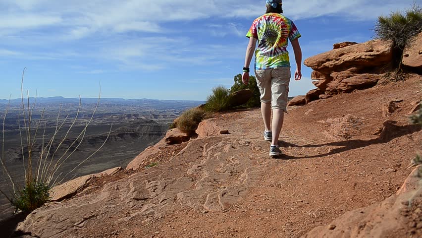 Person hiking along canyon rim on trail looking at scenery