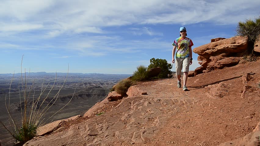 Person hiking along canyon rim on trail looking at scenery
