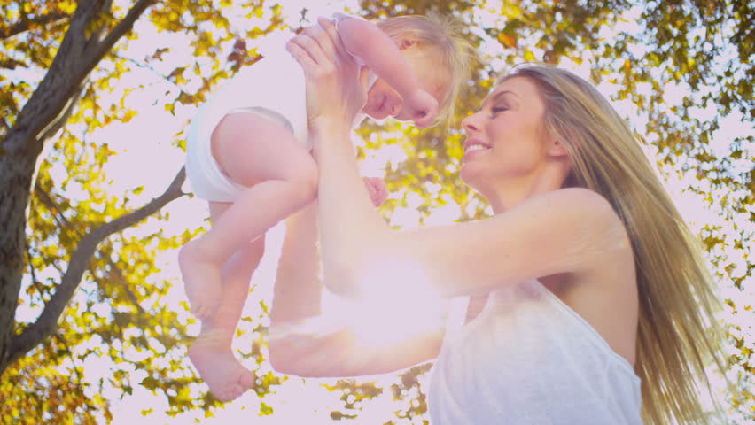 Cute baby being held up high in his beautiful mothers arms outdoors