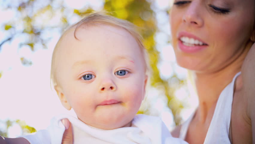 Portrait in close up of young blonde mother outdoors with her smiling baby