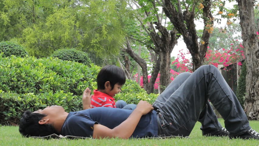 A loving father gives his cute Asian son a big hug and cuddle at the park.