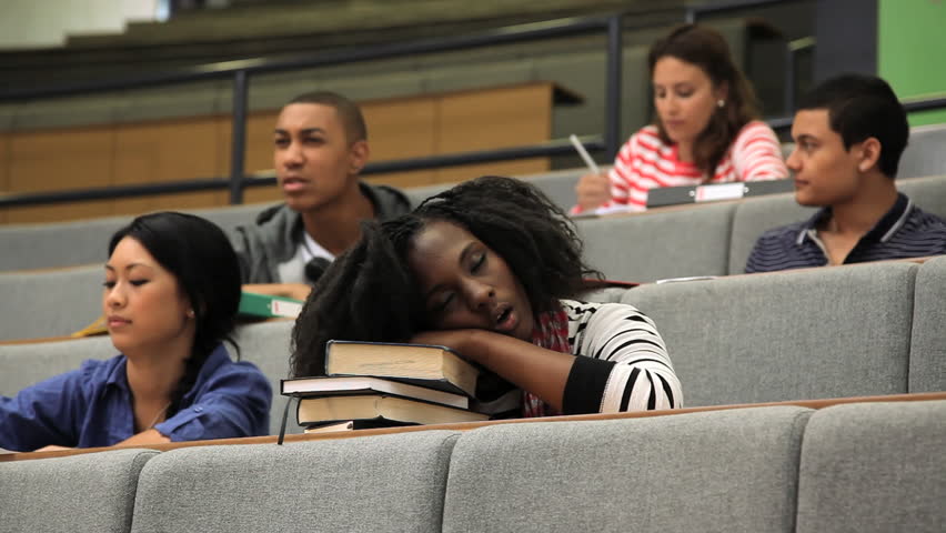 Female student falling asleep on books in lecture theater, during class