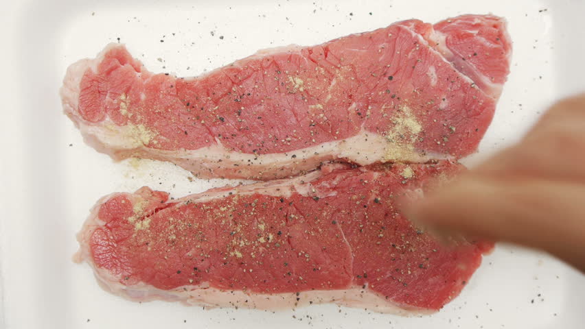 New Your Steaks Seasoned (HD). New York cut beef Steaks beings seasoned with pepper and other spices including garlic, onion and paprika. Seen from the top. 