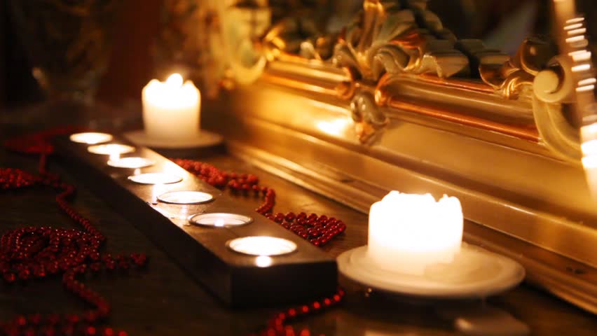 Burning candles and beads face mirror in carved frame in dark