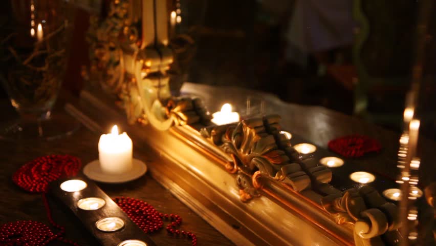Burning candles and beads face a mirror in carved frame