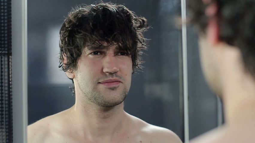 Man wipes his hair with a towel near the mirror