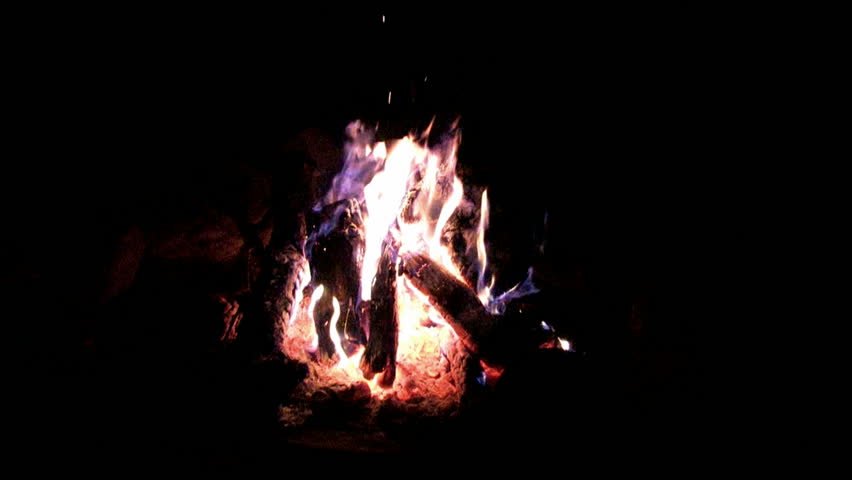 Camp fire with hot fire flames from logs and hot coals. Zoom in. Bonn fire or BBQ pit for cooking and warmth. Flames and smoke dancing around red hot coals and ashes.