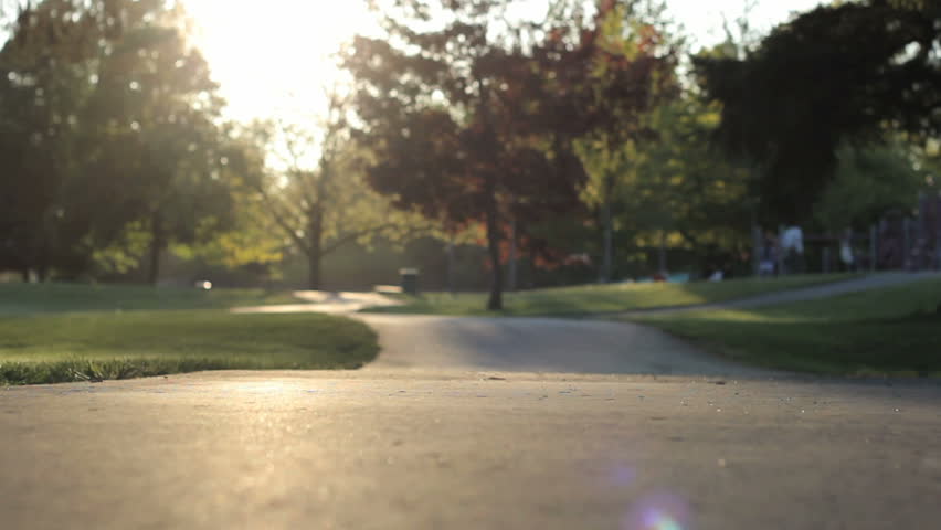 An excited dad helps her young Asian daughter ride her pink bike with training wheels up the hill to the playground.
