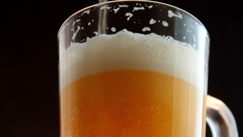 Mug full of beer in glass on a black background. Counter clockwise rotation of beer glass. 