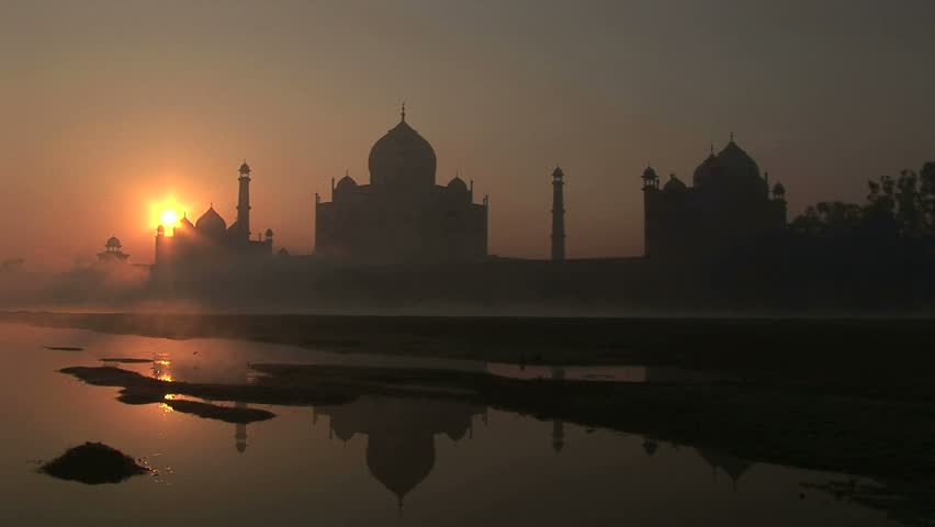 Taj Mahal as sun rises over east end of complex with reflection in river