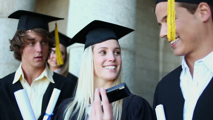 Smiling graduated students photographing themselves in front of the university