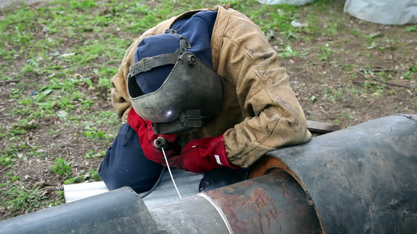 Welding an oil pipeline. Portrait of a welder with protective equipment welding outdoors. HD1080p.