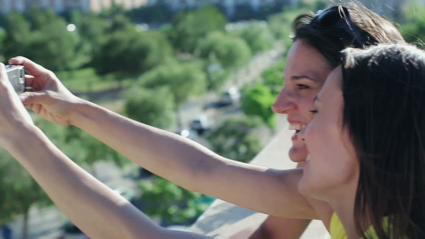 Female friends taking photo with cellphone on balcony
