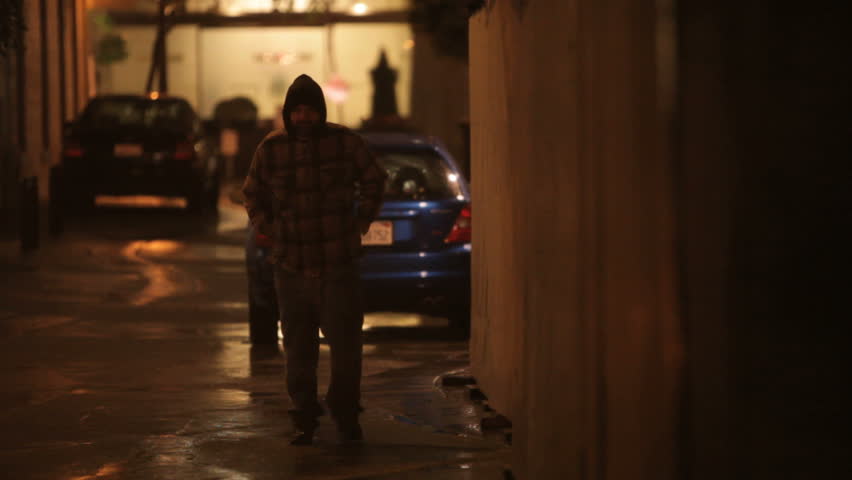 Homeless man walking down an alley on a cold rainy night