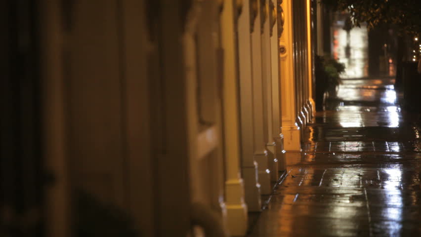 Homeless man walking down the sidewalk at night in the rain