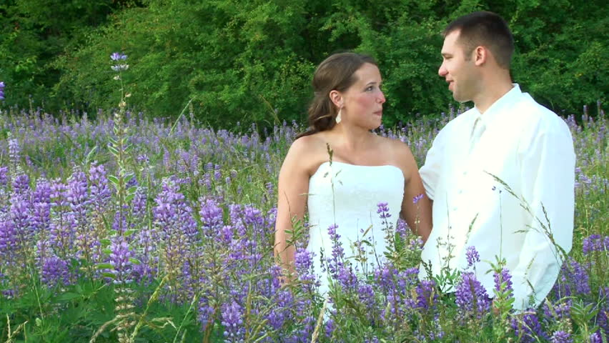 Model released bride and groom smiling on their wedding day during portrait session in beautiful field of violet flowers.