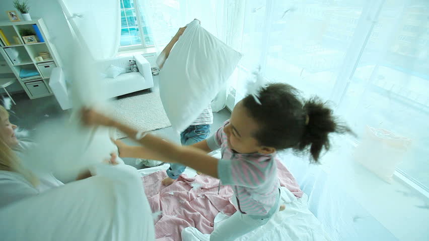 Little friends having an energetic pillow fight with feathers flying all around
