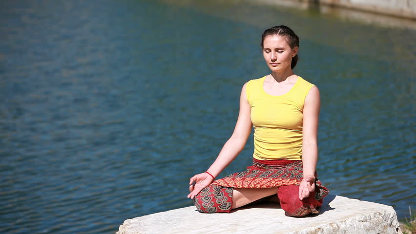Girl sitting on a rock near the water and enjoying harmony with nature
