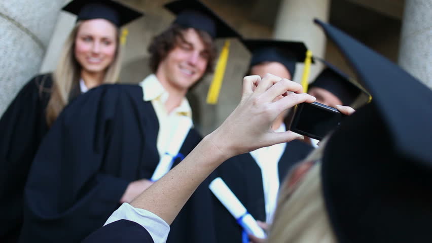 Smiling graduated students being photographed in front of the university
